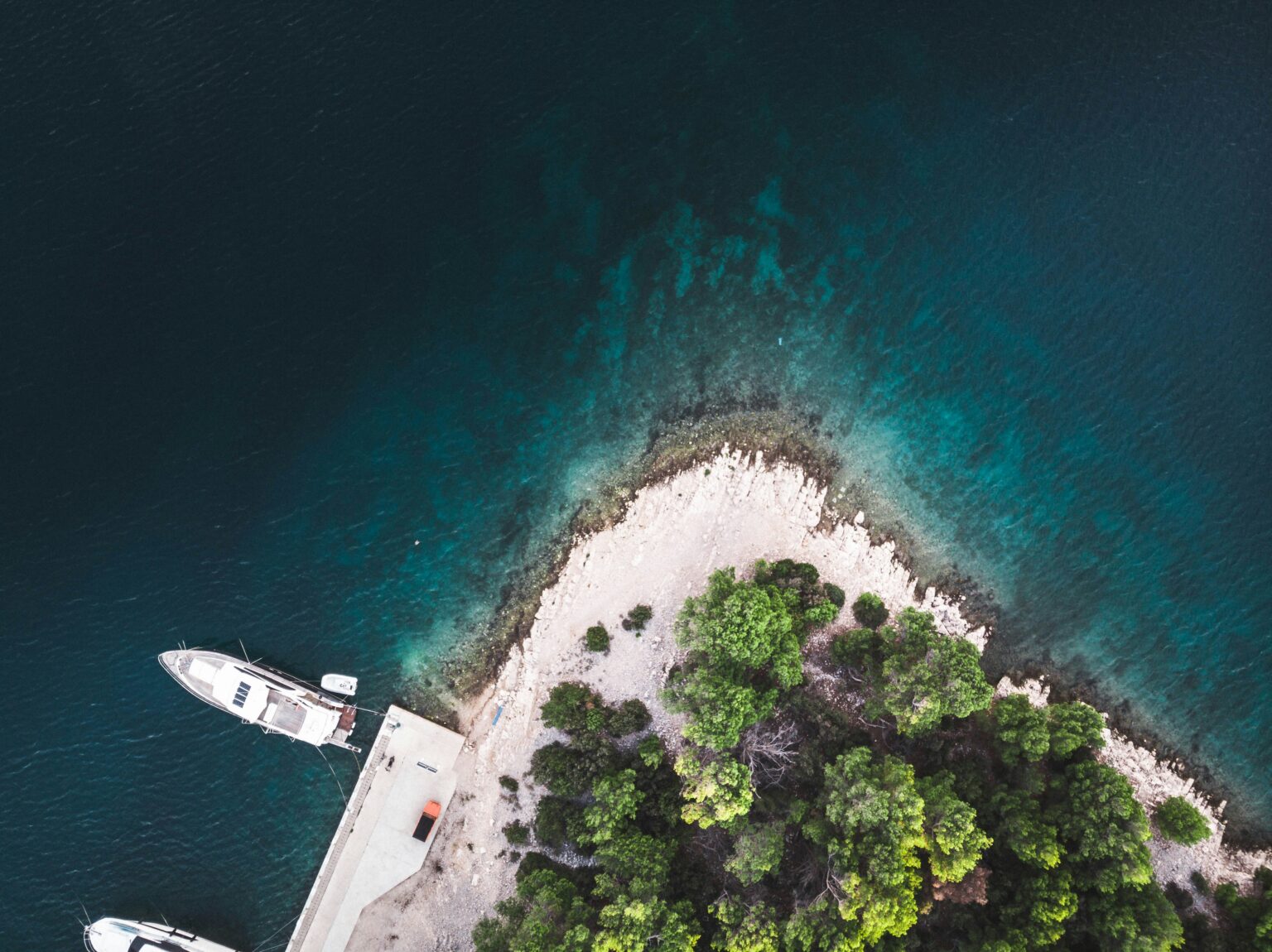 Bewaldete Landzunge mit ankernder Yacht in türkisem Wasser (Luftaufnahme)